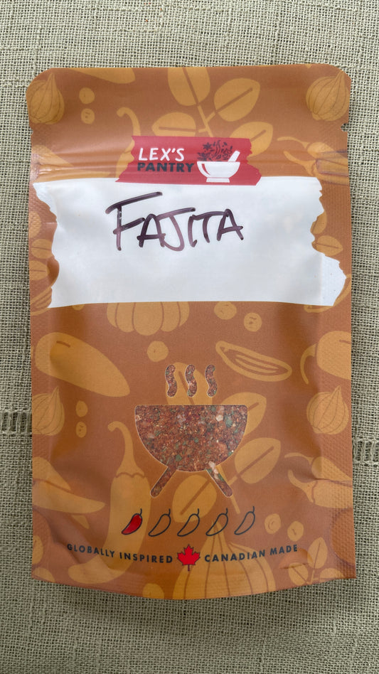 A stand-up pouch of Lex's Pantry Fajita seasoning mix, featuring an kraft-brown pattern of garlic, peppers, spices & herbs. A clear BBQ shaped window showing the mixed seasoning inside. And a white label area with 'FAJITA' hand written in black. The brand logo is red and white, and the packaging is photographed on a textured beige fabric background.