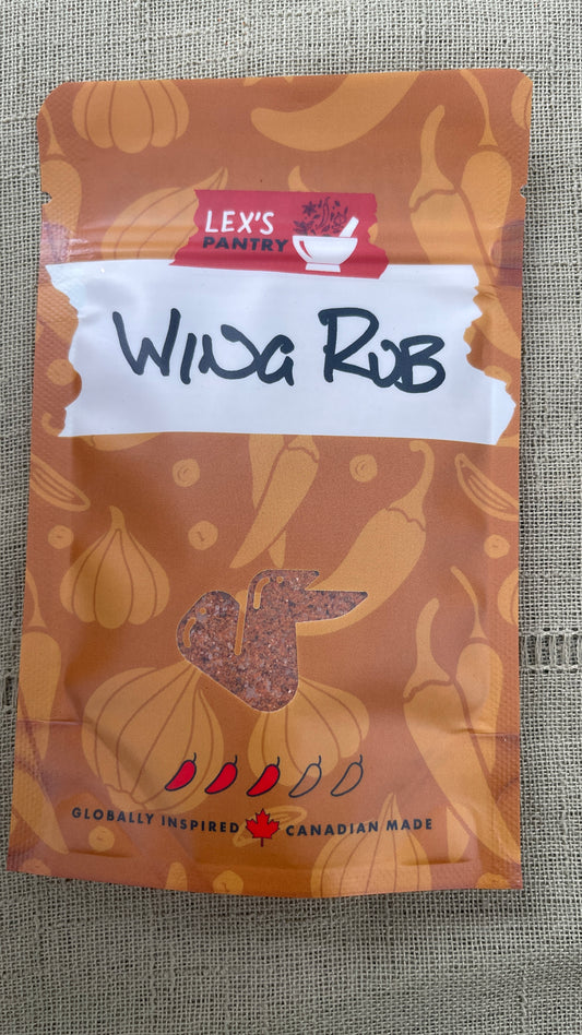 A bag of Lex's Pantry Wing Rub on a textured green fabric background. The packaging is kraft-brown with illustrations of garlic, onions, and chili peppers, featuring a white label with handwritten text. and a clear window shaped like a chicken wing showing thespice blend inside the bag.