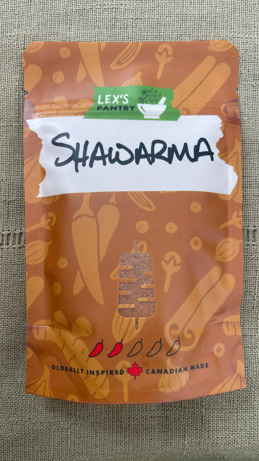 A stand-up pouch package of Shawarma Seasoning by Lex's Pantry, featuring an kraft-brown background with food illustrations, a white banner with the word 'SHAWARMA' in black script, and a green Lex's Pantry logo at the top, photographed on a textured green fabric background.