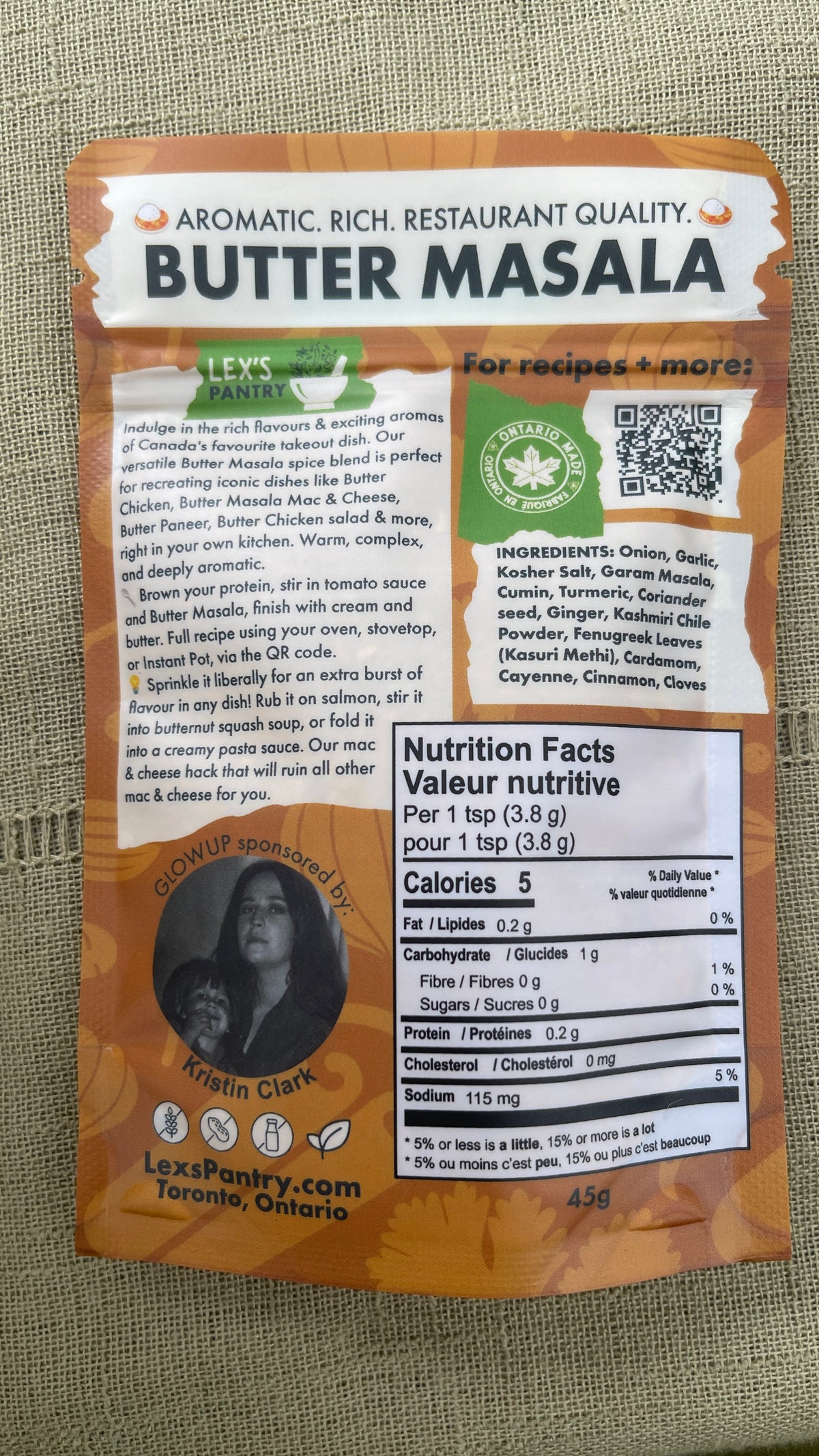 A pouch of Lex's Pantry Butter Masala spice mix, showing the back of the packaging with ingredients, nutrition facts, and a QR code, placed on a textured beige fabric background.
