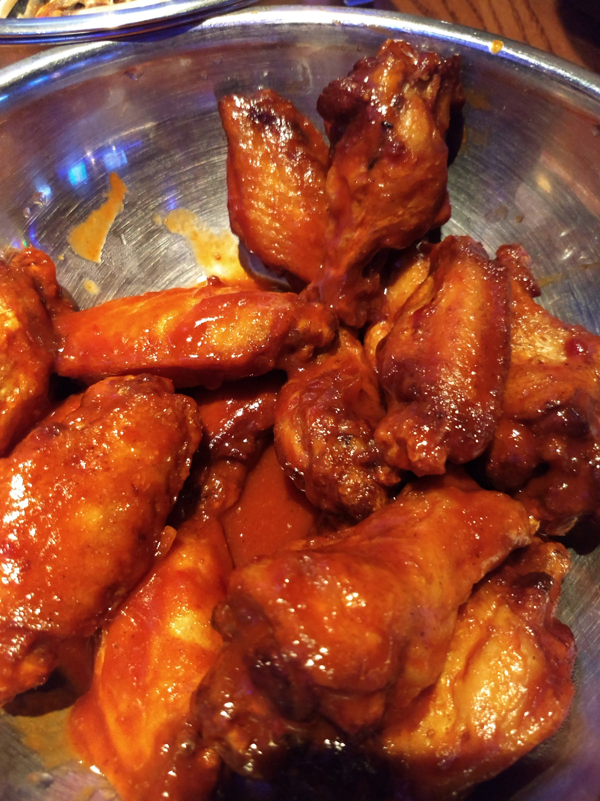Chicken wings in a steel bowl having just been tossed in wing sauce.  