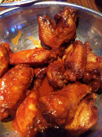 Chicken wings in a steel bowl having just been tossed in wing sauce.  