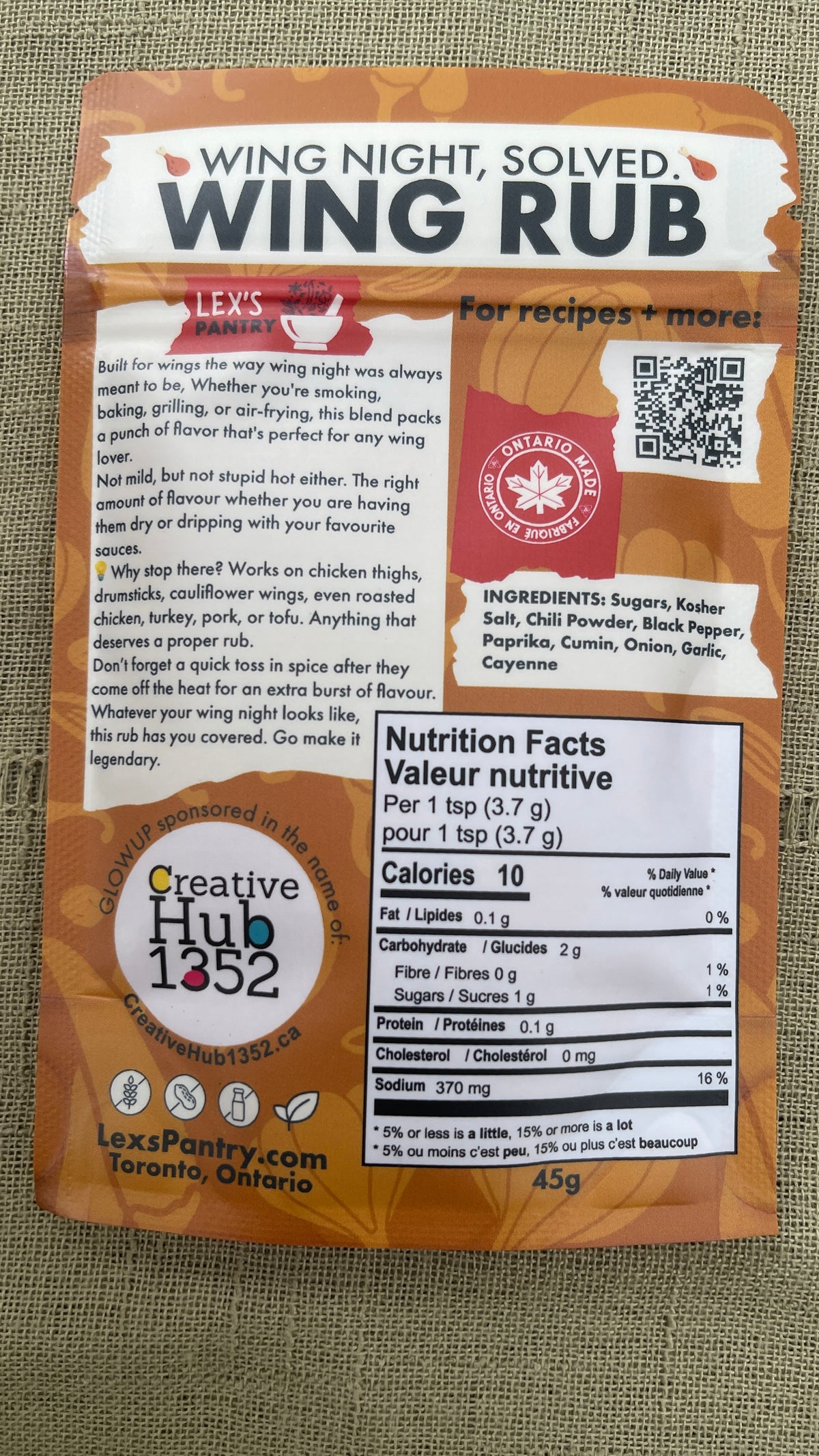 A 45g bag of Lex's Pantry wing rub from behind, featuring a kraft brown design with product details, ingredients, and a nutrition facts label on a textured beige fabric background.