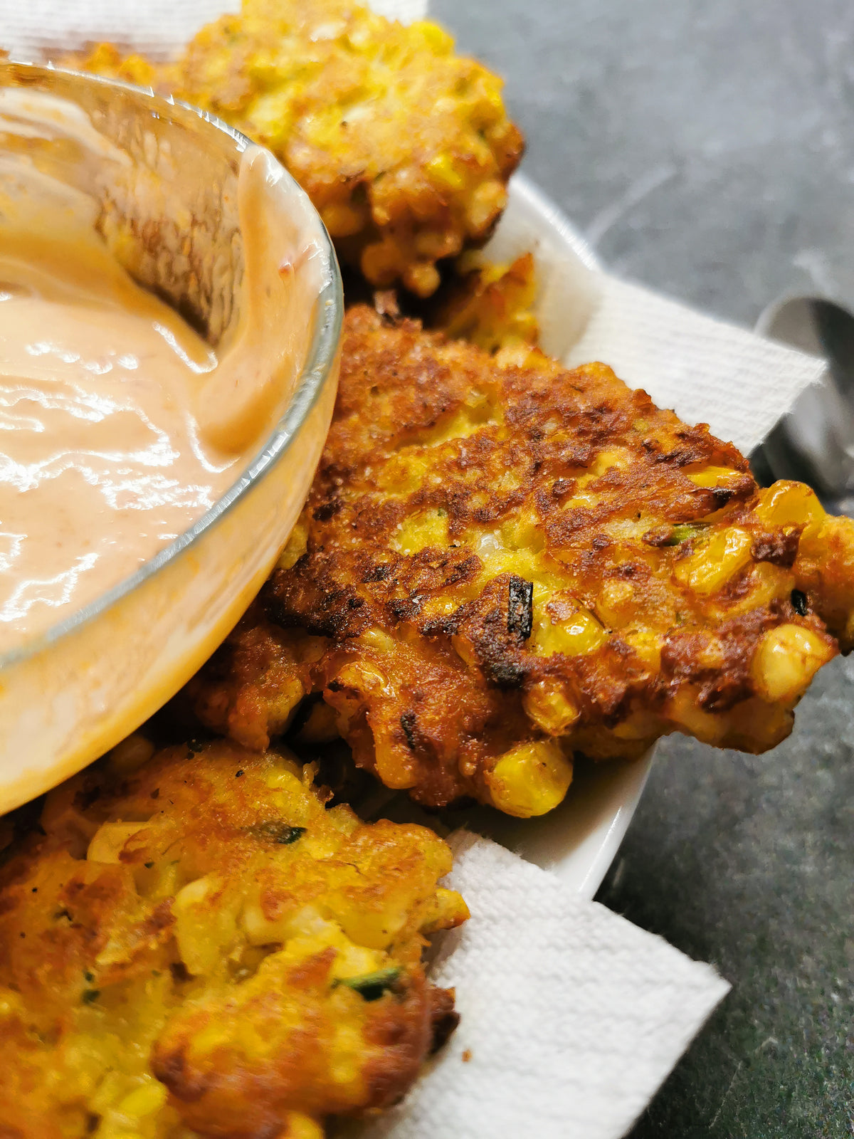 Corn fritters made with Lex's Pantry Montreal Red and a side of dipping sauce made with Montreal Red as well on a paper plate.