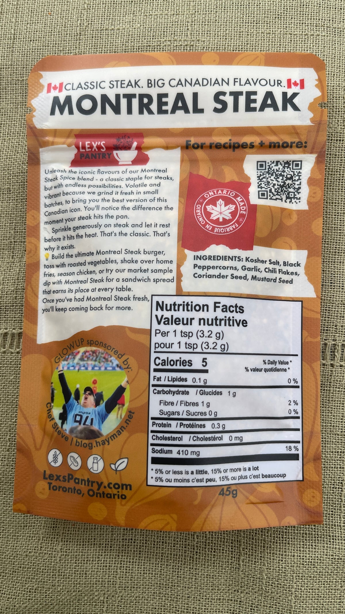 A bag of Lex's Pantry Montreal Steak, featuring a kraft-brown bag with product details, ingredients, and a nutrition facts label, laid flat on a textured green fabric background.