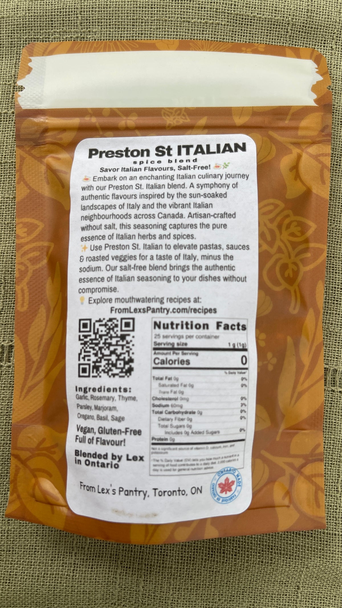 A bag of Preston St Italian seasoning from Lex's Pantry, showing the back label with ingredients, nutrition facts, and a QR code, placed on a textured green fabric background.