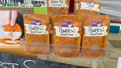 Three bags of Lex's Pantry Pumpkin Spice+Sugar displayed in a clear plastic tray at an outdoor market.
