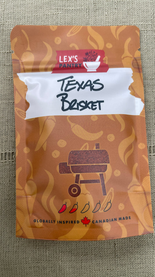 A stand-up pouch of Lex's Pantry Texas Brisket Seasoning and Rub, featuring an Kraft-brown patterned design with a white banner and a barbecue grill clear window showing the spice in the package, placed on a textured green fabric background.