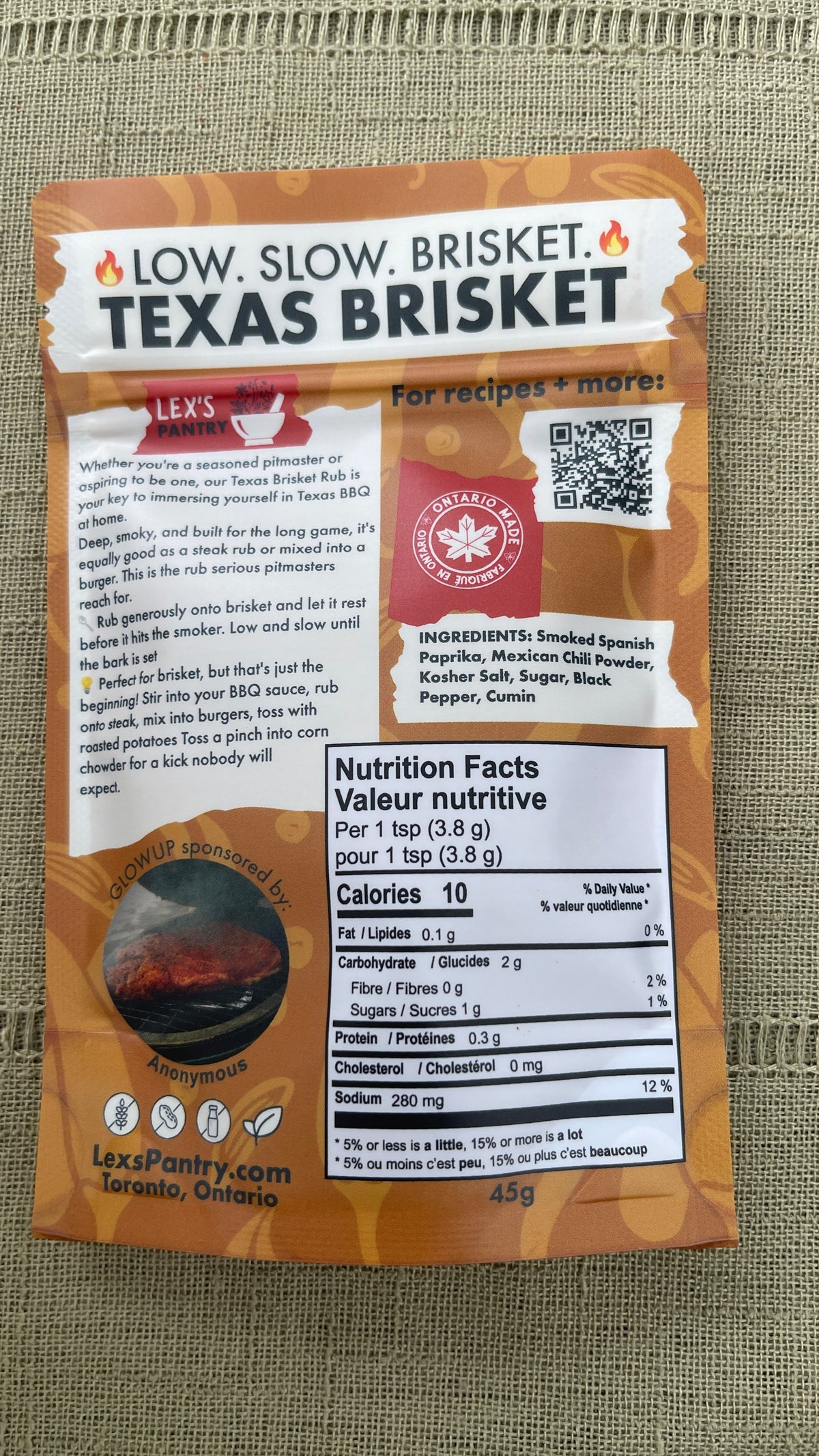 Back of a Texas Brisket package from Lex's Pantry, showing flavour text, ingredients, nutrition facts, and a QR code on a textured green fabric background.