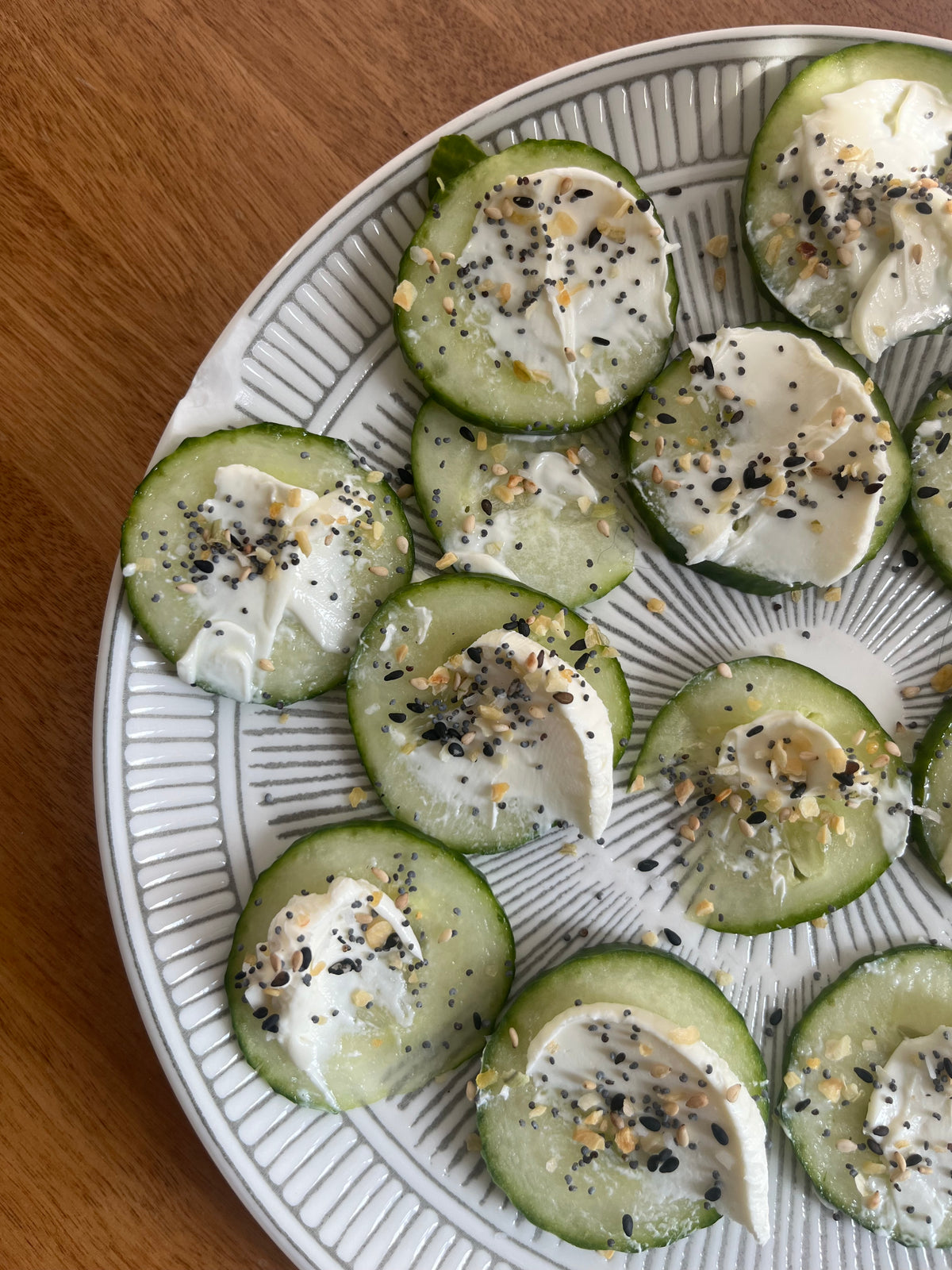 Cucumber slices with cream cheese and Lex's Pantry Everything Bagel seasoning on a decorative plate.