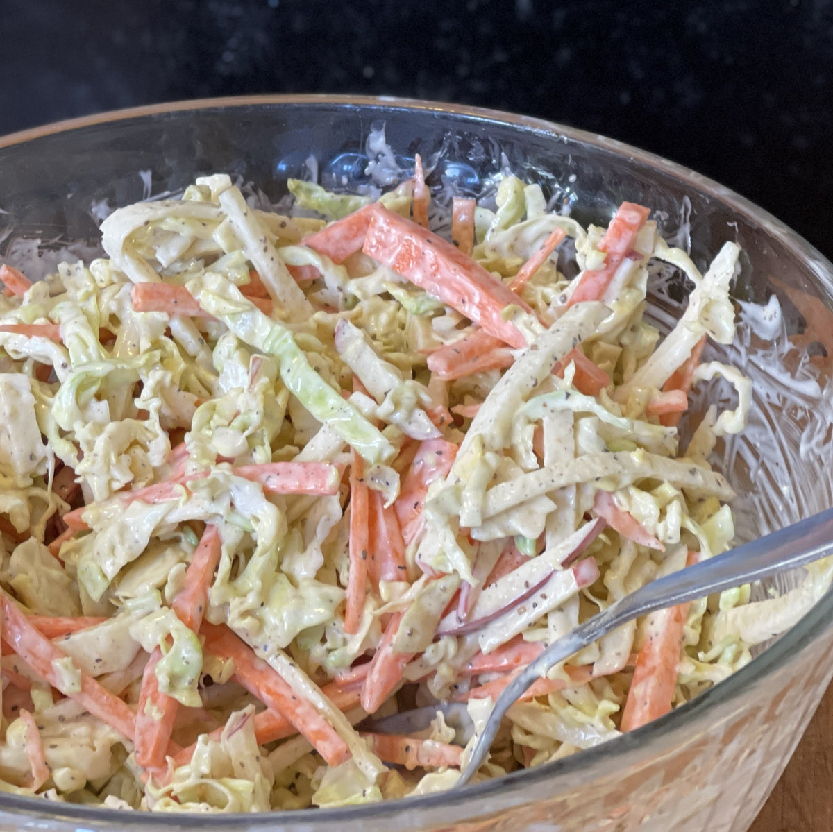 Glass bowl with coleslaw made with Memphis Zero and a spoon on a wooden surface.