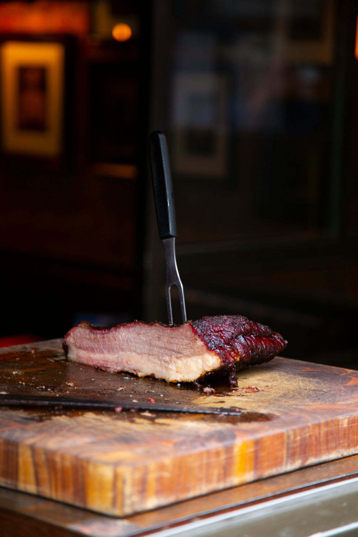 Sliced brisket make with Lex's Pantry Texas Brisket Rub on a wooden cutting board with a knife, in a dimly lit setting.