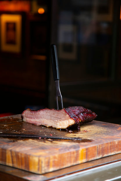 Sliced brisket make with Lex's Pantry Texas Brisket Rub on a wooden cutting board with a knife, in a dimly lit setting.