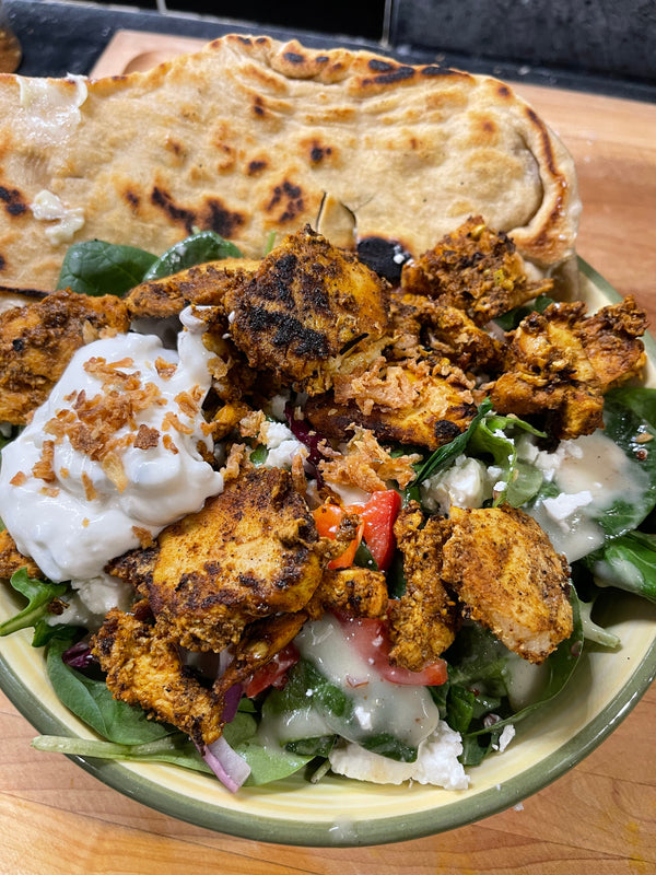 A plate of chicken shawarma made with Lex's Pantry Shawarma Spice & Seasoning Blend with salad and yogurt, alongside flatbread.